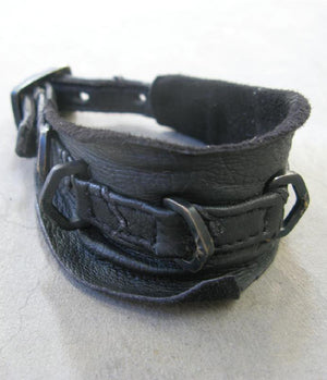Black leather cuff with metal buckle on a light gray background