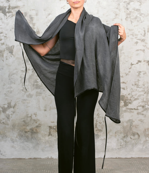 Person wearing a gray linen scarf over a black outfit against a textured wall.