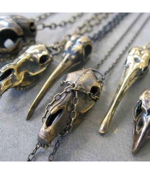 Bronze horse skull & bird skull pendants on chains against a gray background