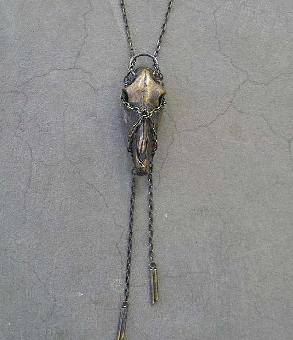 A brass horse skull necklace with antiqued brass chain laid out on a textured surface.